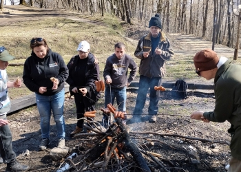 Uczestnicy wycieczki pieką kiełbaski nad ogniskiem.