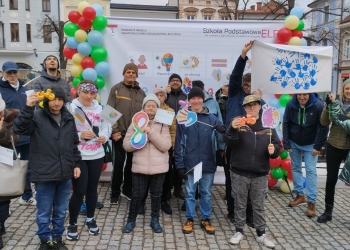 Uczestnicy marszu pozyja do wspólnej fotografii. Trzymają w rękach kolorowe emblematy oraz flagę okolicznościową.