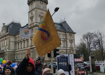 Uczestnicy marszu trzymając w rękach flagę, pozują do fotografii na tle Ratusza.