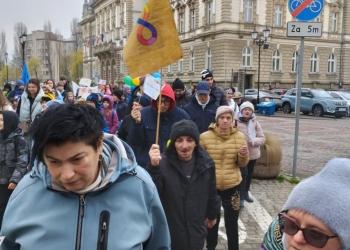 Uczestnicy marszu trzymając w rękach flagę, pozują do fotografii na tle Ratusza.