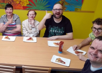 Uczestnicy spotkania siedzą dookoła stołu. na stole sa przygotowane talerze.