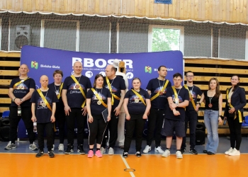Na zdjęciu znajduje się jedna z drużyn. Osoby maja na sobie czarne podkoszulki i żólte szarfy.