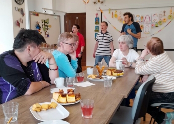 Uczestnicy spotkania siedza przy stole, rozmawiają. Na stole są słodycze i napoje.