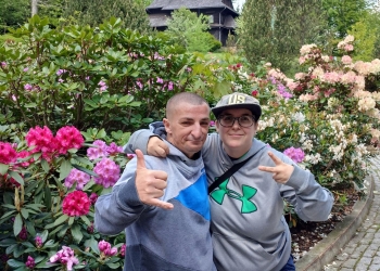 Uczestnicy wycieczki pozują do fotografii. W tle kwitnace rododendrony, w oddali budynek rezydencji.