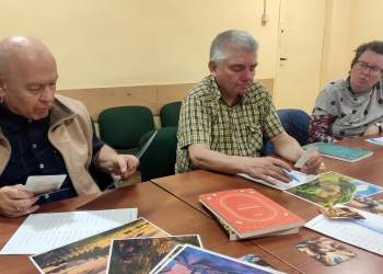 Uczestnicy siedzący przy stole wybierają z kolorowych obrazków te, które będa przydatne do wspólnego opowiadania.
