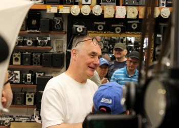 Przewodnik opowiada o historii fotografii, o sprzęcie fotograficznym. w tle zabytkowe aparaty fotograficzne.
