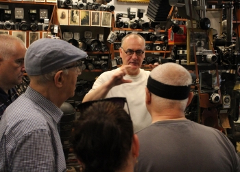 Przewodnik opowiada o historii fotografii, o sprzęcie fotograficznym. w tle zabytkowe aparaty fotograficzne.