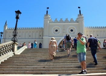 Uczestnik wycieczki pozuje do zdjęcia stojąc na schodach prowadzących do zamku lubelskiego.