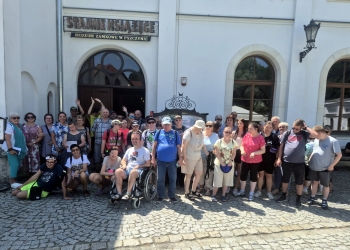 Uczestnicy wycieczki pozują do zdjęcia stojąc przed budynkiem pałacu pszczyńskiego.