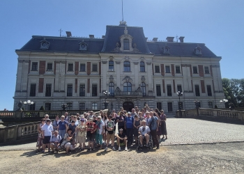 Uczestnicy wycieczki pozują do zdjęcia stojąc przed budynkiem pałacu pszczyńskiego.