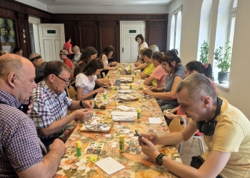 Uczestnicy siedzą przy stole, przygotowując pocztówkę.