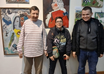 Uczestnicy podczas zwiedzania pozują do zdjęcia. W tle na scianie wiszą obrazy.