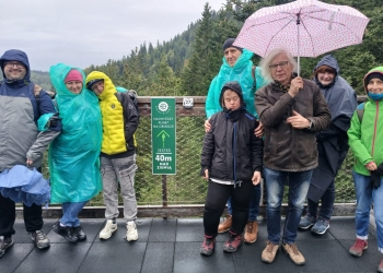 Grupa uczestników wycieczki podczas spaceru ścieżką w koronach drzew. Pada deszcz. 