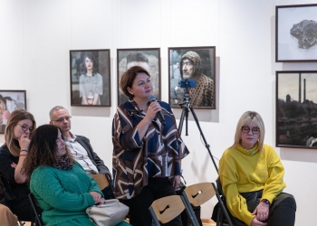 Dyrektor ŚDS PODKOWA uczestniczy w spotkaniu, w ręku trzyma mikrofon. W tle na scianach fotografie.