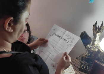 Uczestniczka spotkania odczytuje z kartki treść zagadki. w tle swiecąca się lampka w kształcie smoka.