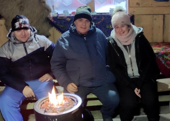 Uczestnicy kuligu pozują do zdjęcia siedząc obok ogniska.