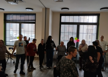 Uczestnicy zabawy tańczą trzymając się za ręce. W tle jest duże, jasne okno.