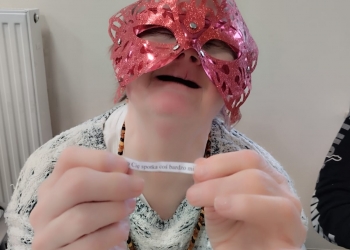 Uczestniczka zabawy trzyma w dłoniach małą karteczkę z napisem dziś spotka cię coś miłego. Na twarzy ma błyszczącą maskę.