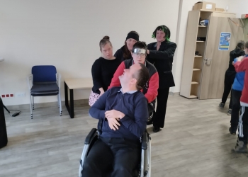 kilka osób podcza wspólnej zabawy tworza korowód. Jeden z uczestników siedzi na wózku inwalidzkim.