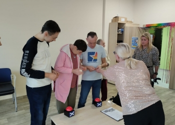 Kilku uczestników podczas konkursu.Uczestnicy odczytują pytania z kartki, na stoliku znajdują się dwa przyciski.