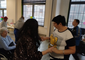 Kilka osób tańczy, Jedna z osób - kobieta - siedzi na wózku inwalidzkim.