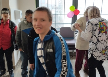 Kilka osób tańczy w parach, na pierwszym planie młody mężczyzna uśmiecha sie patrząc prosto w obiektyw aparatu.