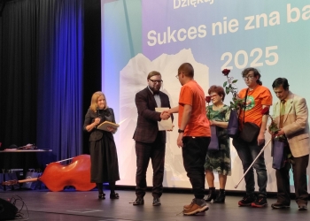 Zastępca prezydenta miasta Bielska-Białej wręcza dyplom wyróżnienia uczestniczłonkowi Klubu Górskiego. Uczestnik ma na sobie pomarańczową koszulkę. w tle baner nawiązujący do treści konkursu.