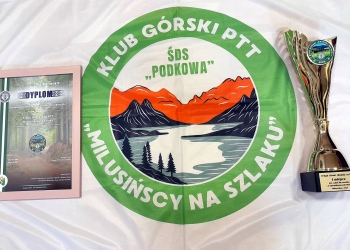 Zdjęcie przedstawia logo Klubu Górskiego Milusińscy na szlaku, z lewej strony znajduje się dyplom, z prawej strony jest puchar.