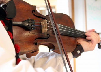 zdjęcie przedstawia skrzypce i smyczek oraz dłoń grającego.