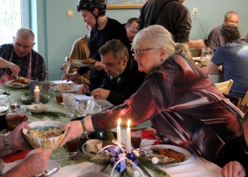 Wspólny posiłek. Na stole są potrawy oraz świąteczne stroiki, są zapalone świece.