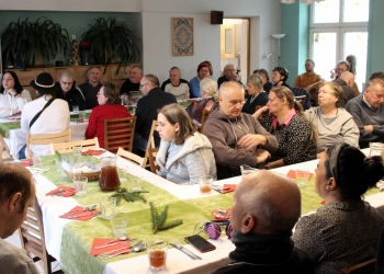 Uczestnicy spotkania siedzą przy stole. Stół jest świątecznie udekorowany.