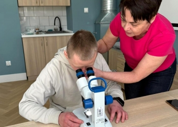 Osoba na zdjęciu ogląda przez mikroskop krople wody. Osobie pomaga instruktorka.