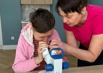 Osoba na zdjęciu ogląda przez mikroskop krople wody. Osobie pomaga instruktorka