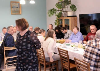 Zdjęcie przedstawia grupę osób zgromadzonych przy długim stole.