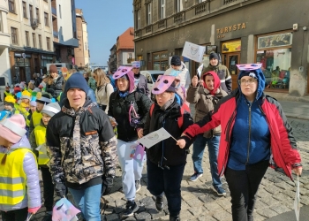 Na zdjęciu znajdują się osoby świętujące Światowy Dzień Świadomości Autyzmu i biorące udział w marszu. W rękach trzymają emblematy nawiązujące tematycznie do tego wydarzenia.