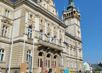 Zdjęcie przedstawia osoby zgromadzone przed budynkiem ratusza. W rękach trzymają rekwizyty nawiazujące do emocji.