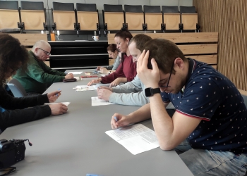 Osoby siedzące dookoła szarego stołu wypełniaja ankietę dotyczącą optymizmu i pesymizmu.