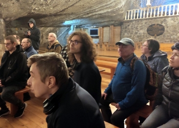 Uczestnicy wycieczki znajdują się w kaplicy, siedzą na niskich ławkach.