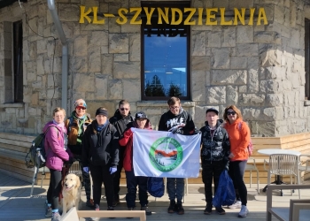 Na zdjęciu widać grupę osób stojących przed budynkiem kolejki górskiej Szyndzielnia. Wśród osób znajduje się duży, jasny pies.