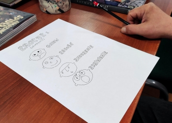 Na zdjęciu widoczna jest kartka z narysowanymi emotikonami przedstawiającymi różne emocje: gniew, radość, znudzenie i zdziwienie. Kartka leży na stole obok komiksów i przyborów do rysowania. 